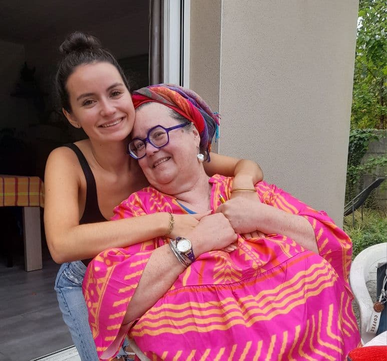 Une jeune de Généraction et une sénior, souriantes et enlacées sur une terrasse.